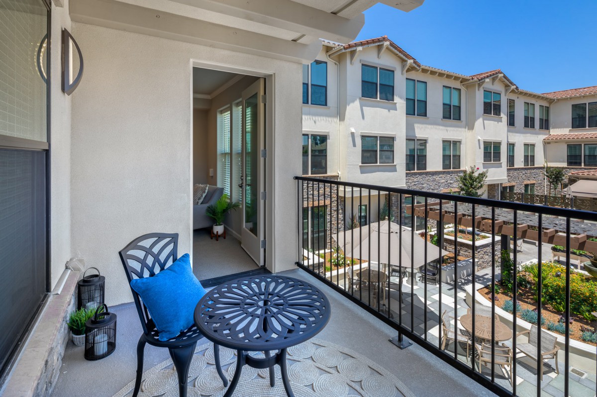 A cozy apartment balcony with a small table and chairs overlooking a courtyard.