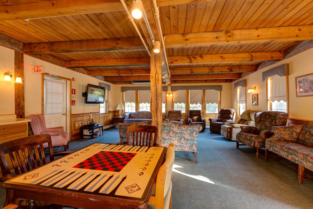 A cozy, rustic-style living room with wooden ceilings, comfortable seating, and a game table.