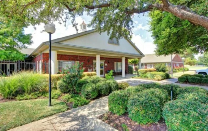 A well-maintained building entrance surrounded by lush landscaping and a paved pathway.