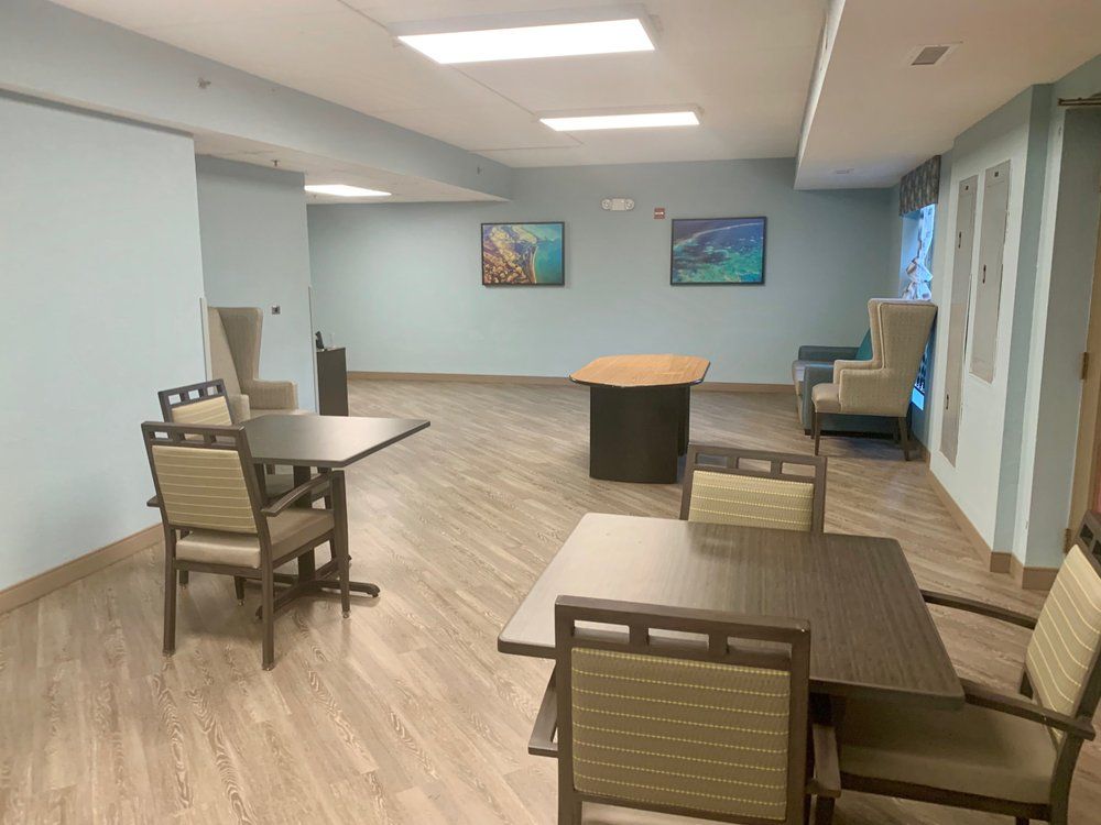 A modern, spacious room with tables and chairs, featuring a wooden floor and contemporary lighting.