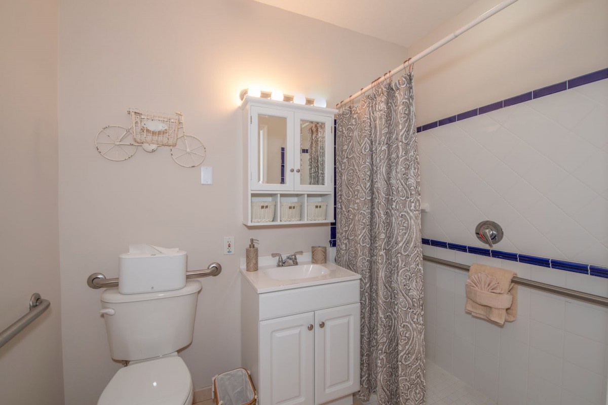 A small bathroom featuring a toilet, sink with a mirror cabinet above, and a shower area with a patterned curtain.