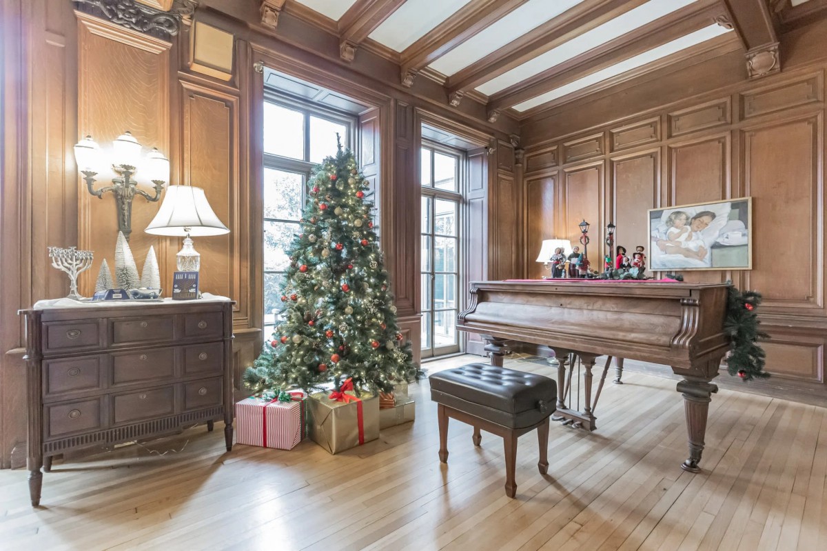 A cozy living room decorated for Christmas with a piano, holiday tree, and wrapped gifts.