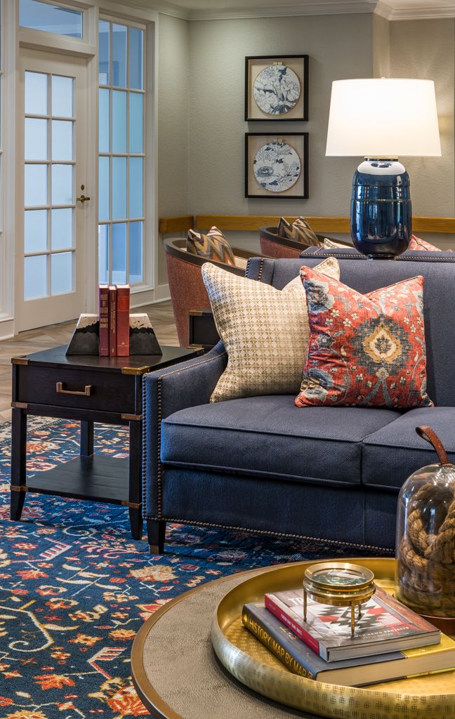 A cozy living room setting featuring a navy sofa adorned with decorative pillows, a side table with books and a lamp, and various home decor elements.