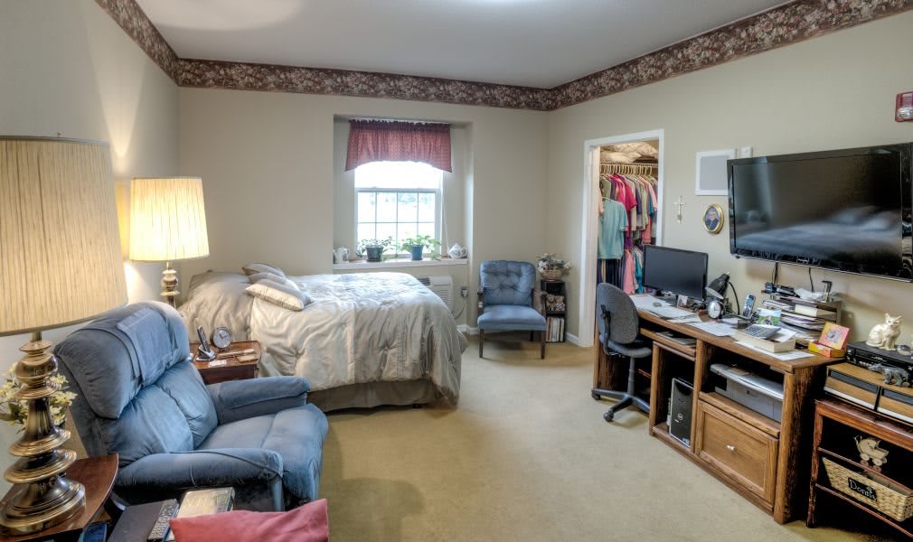 A cozy bedroom featuring a bed, desk, and seating area with a window and closet.