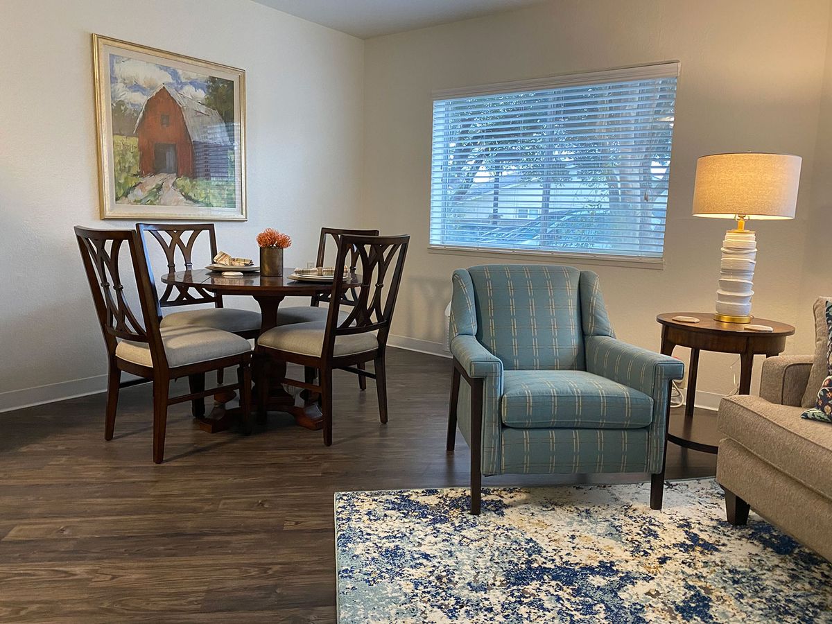 A cozy corner featuring a dining table set, an armchair, and a side table with a lamp in a well-lit living space.
