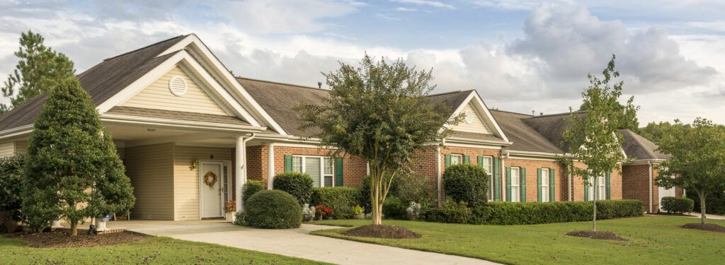 A suburban brick house with well-maintained landscaping and a tree in the front yard.