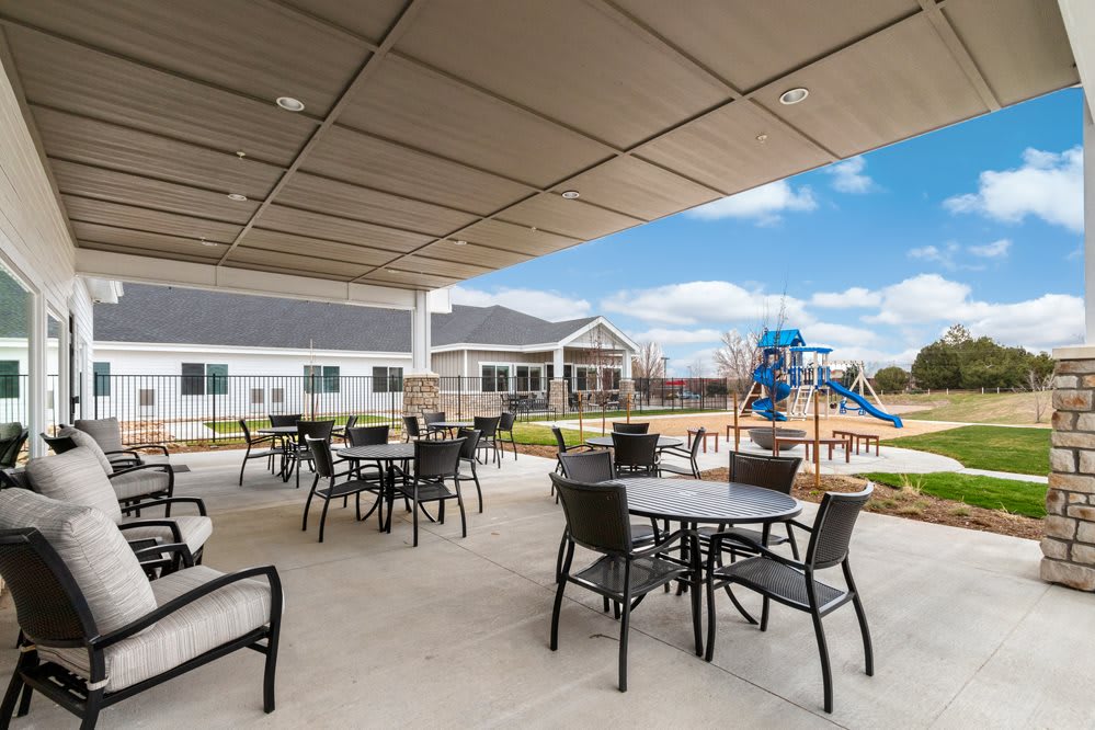 A spacious outdoor patio with tables and chairs, adjacent to a playground in a residential setting.