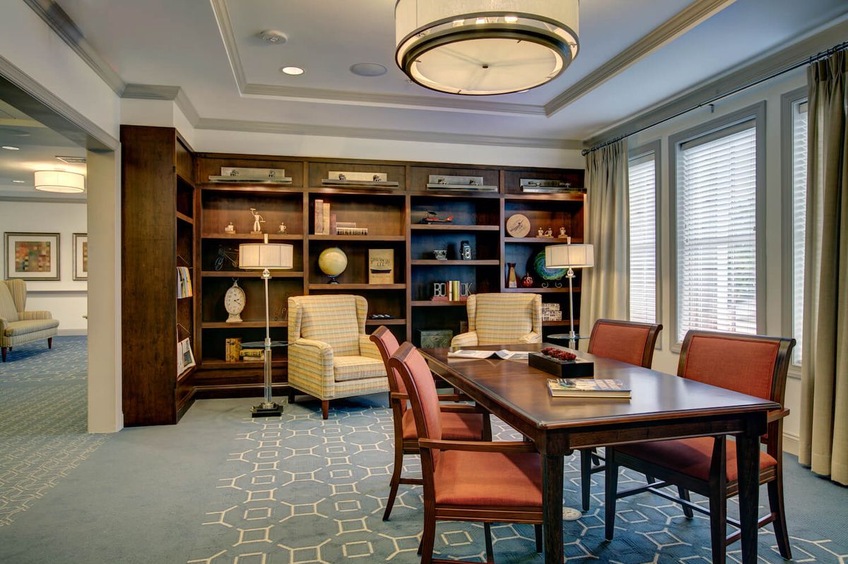 A well-furnished library with a large meeting table, surrounded by bookshelves and comfortable seating.