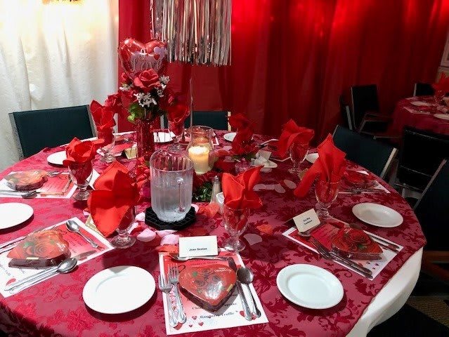 A beautifully decorated dining table with a red theme, featuring elegant table settings and a floral centerpiece.