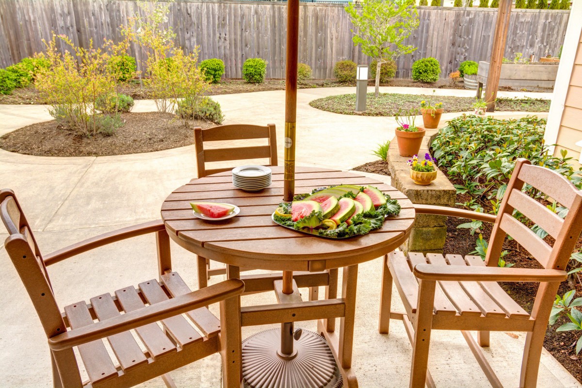 A cozy backyard patio with a wooden table set for a meal, surrounded by plants.