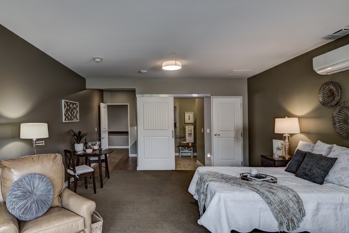 A modern bedroom with stylish furnishings, including a bed, chair, table, and lamp.