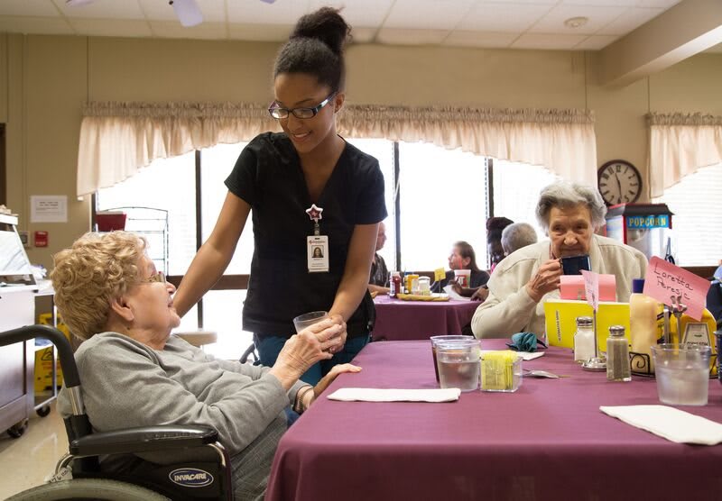 A caregiver assists an elderly woman in a nursing home setting, providing support and companionship.