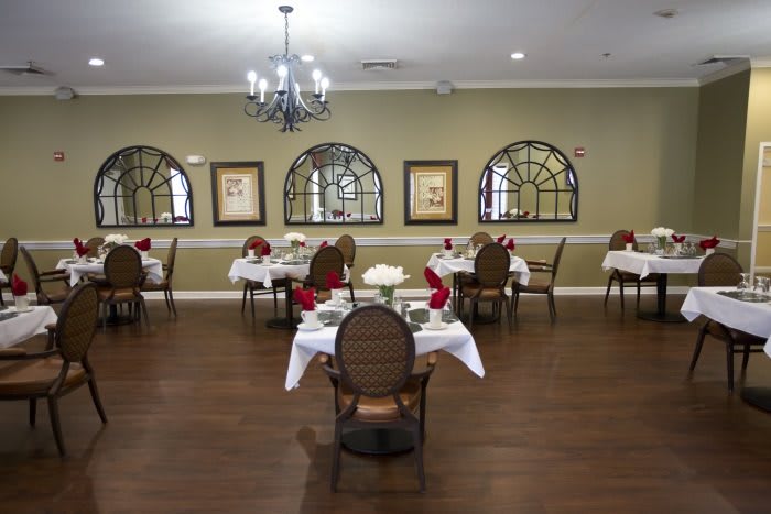 An elegant dining room with neatly arranged tables and chairs, decorated with mirrors and a chandelier.