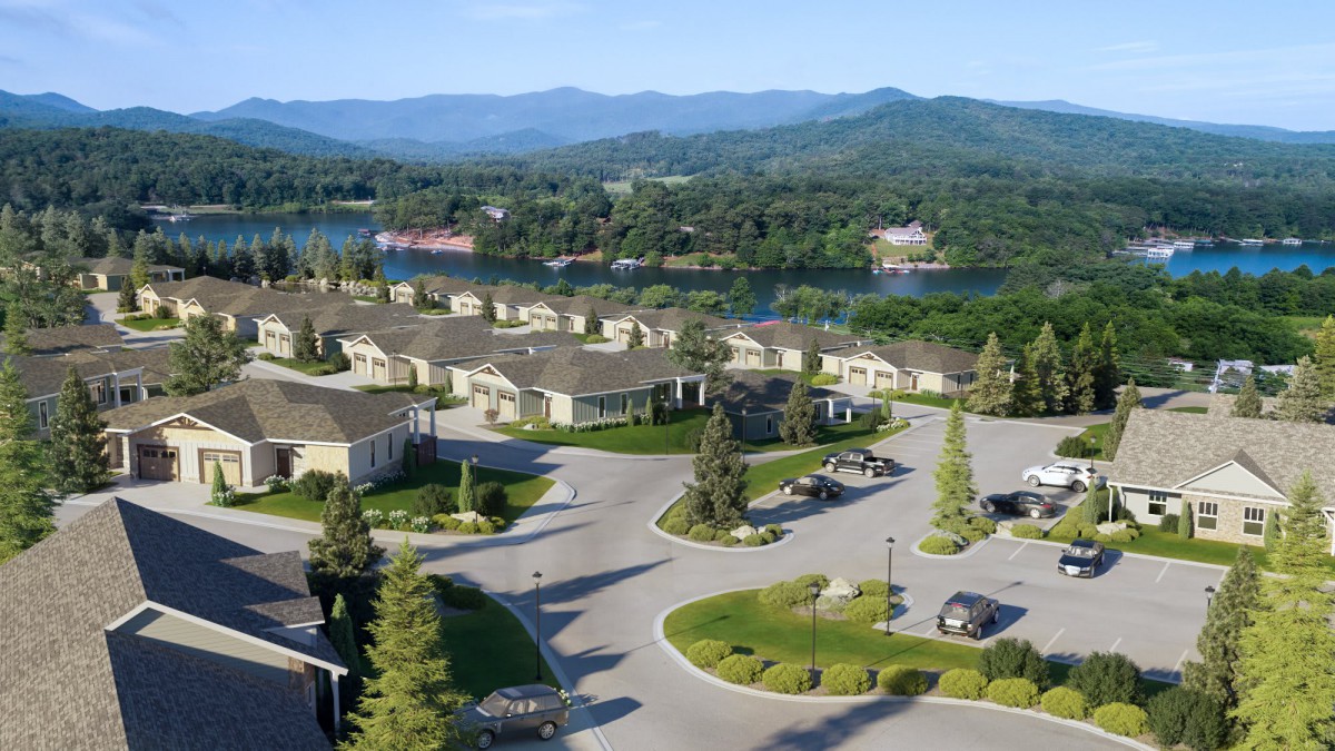 A scenic aerial view of a residential area with houses, surrounded by trees, a lake, and mountains in the background.