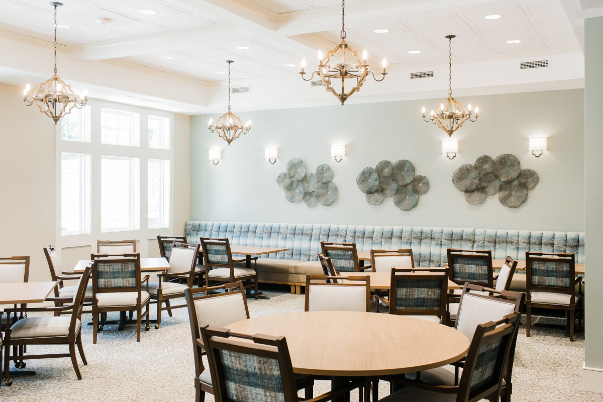 A well-lit dining area with round tables, chairs, chandeliers, and decorative wall art.