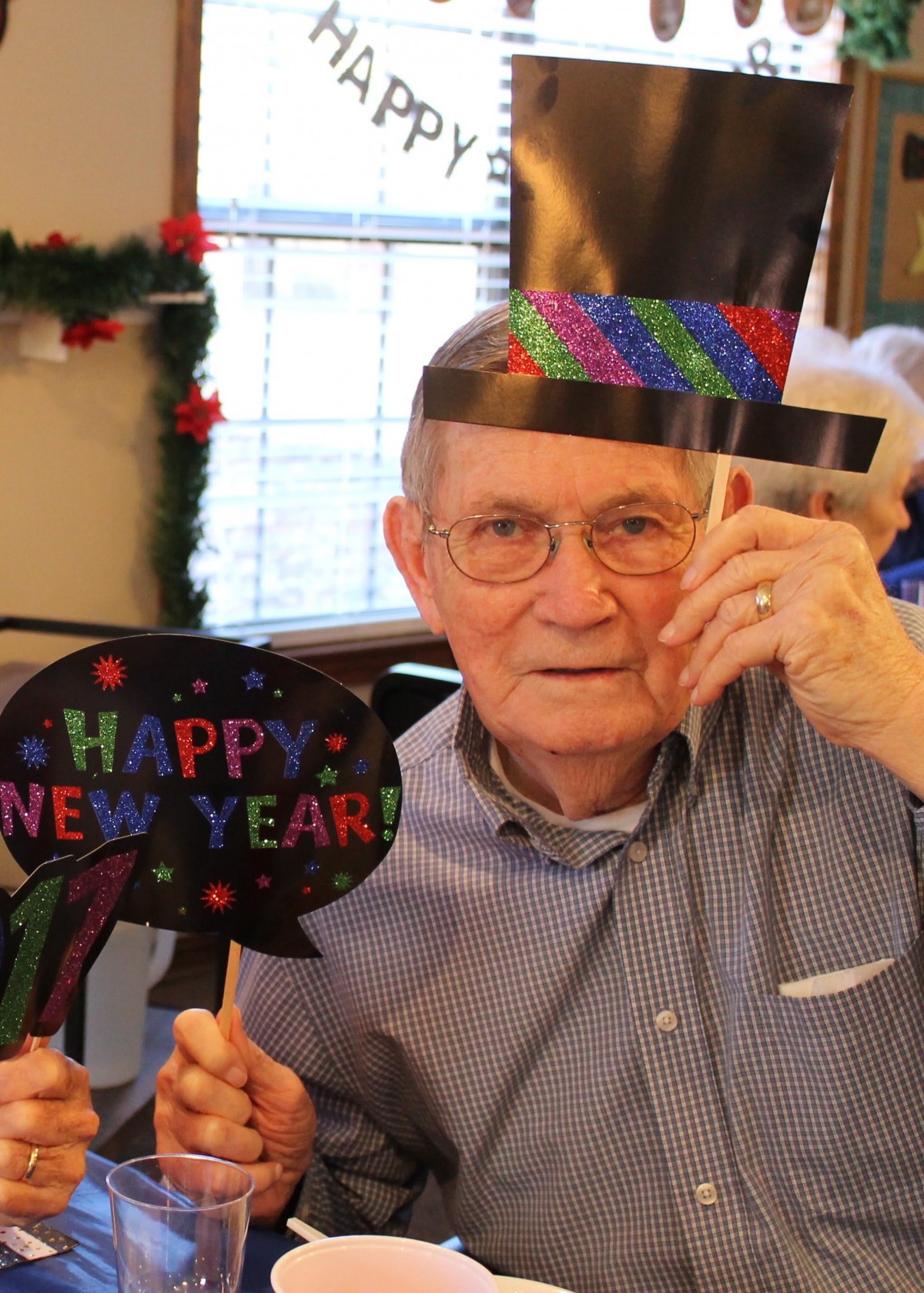 An elderly person celebrating New Year with festive decorations and a party hat.