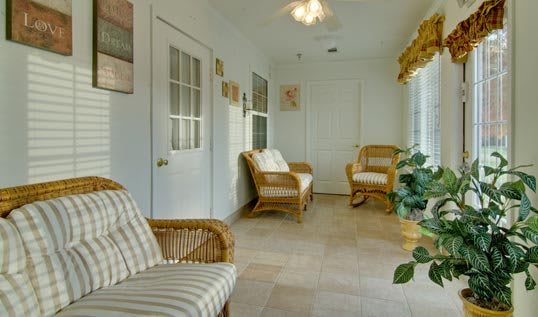 A cozy sunroom with wicker chairs, tiled flooring, and large windows.