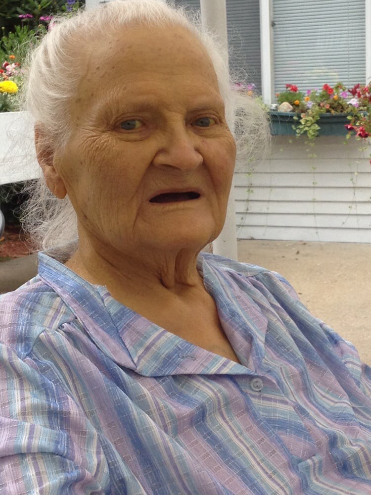 An elderly woman sitting outdoors with a calm expression.