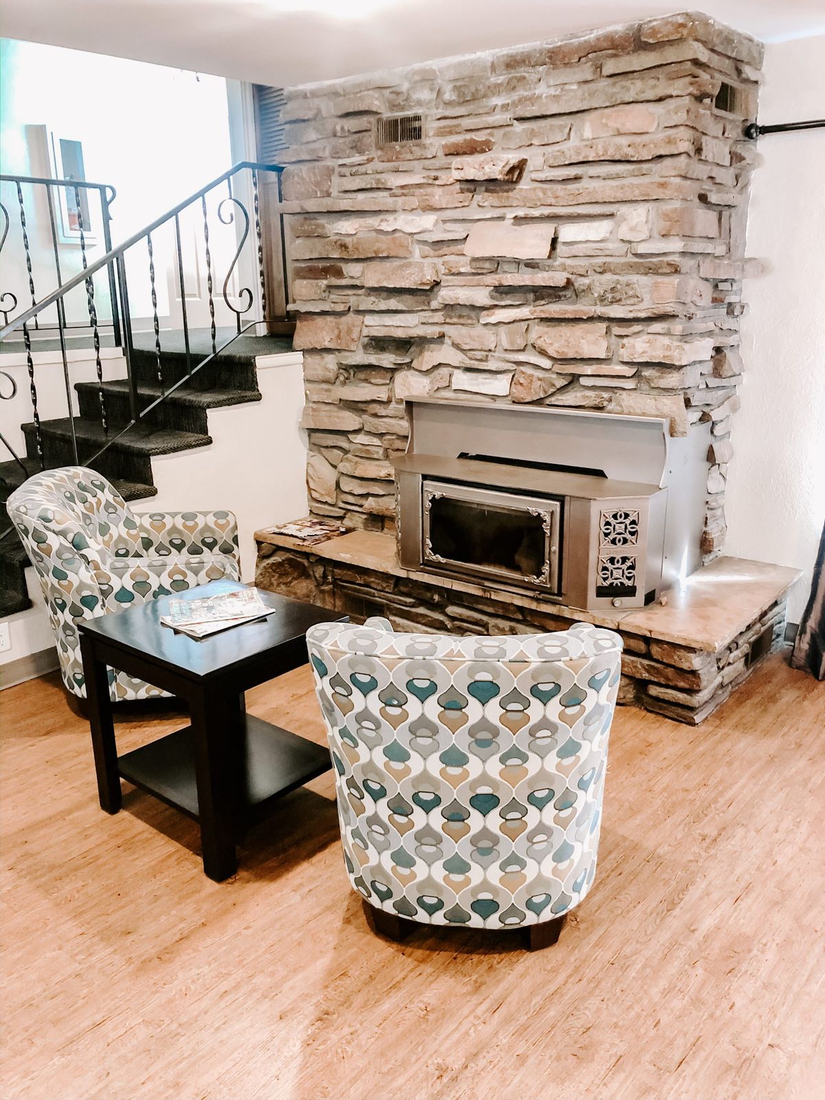 A cozy living room with a stone fireplace, patterned armchairs, and wood flooring.