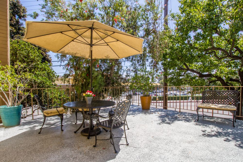 A sunny outdoor patio with a table, chairs, and a large umbrella surrounded by trees.