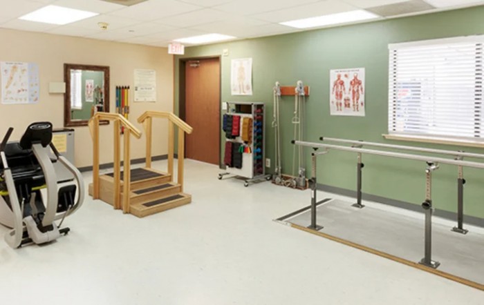 A rehabilitation room equipped with physical therapy equipment including parallel bars and a staircase.