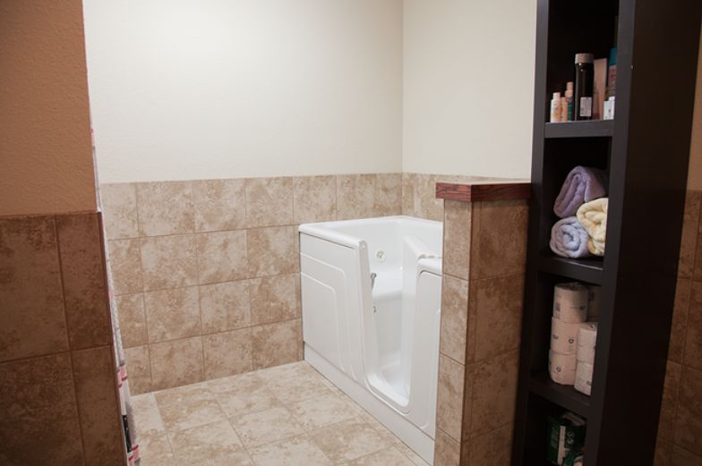 A well-designed bathroom featuring a walk-in tub and tiled walls, with a shelf stocked with towels and toiletries.