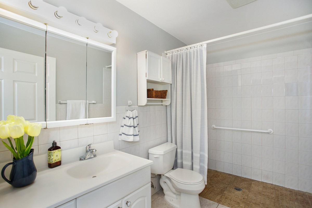 A modern bathroom with white decor, featuring a sink, toilet, and shower area.