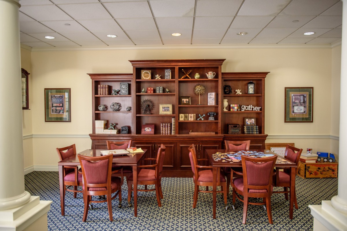 A well-furnished library room featuring wooden bookshelves, tables, and chairs.