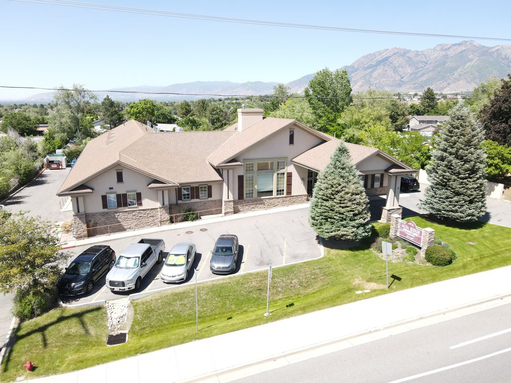 A suburban house with a driveway, several cars parked, and a scenic mountain backdrop.