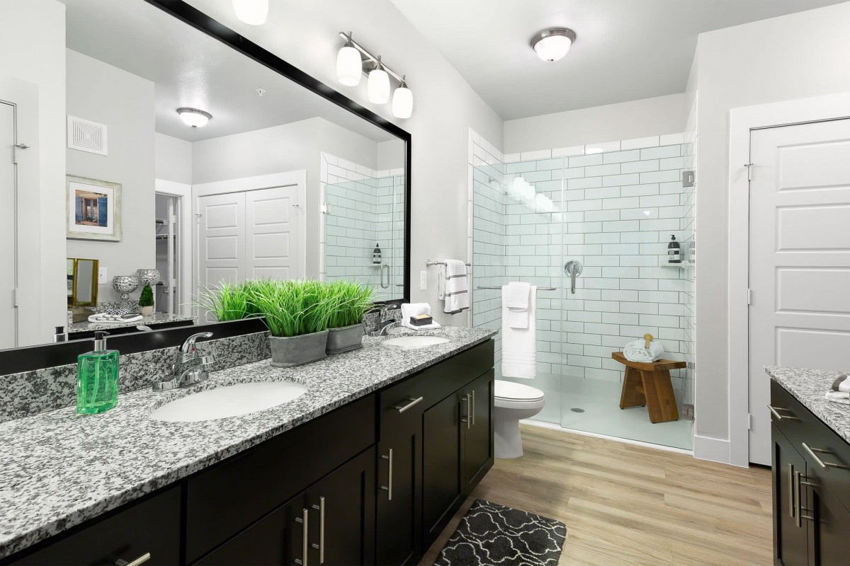 A modern bathroom featuring a large mirror, granite countertop, and a walk-in shower with white tile walls.