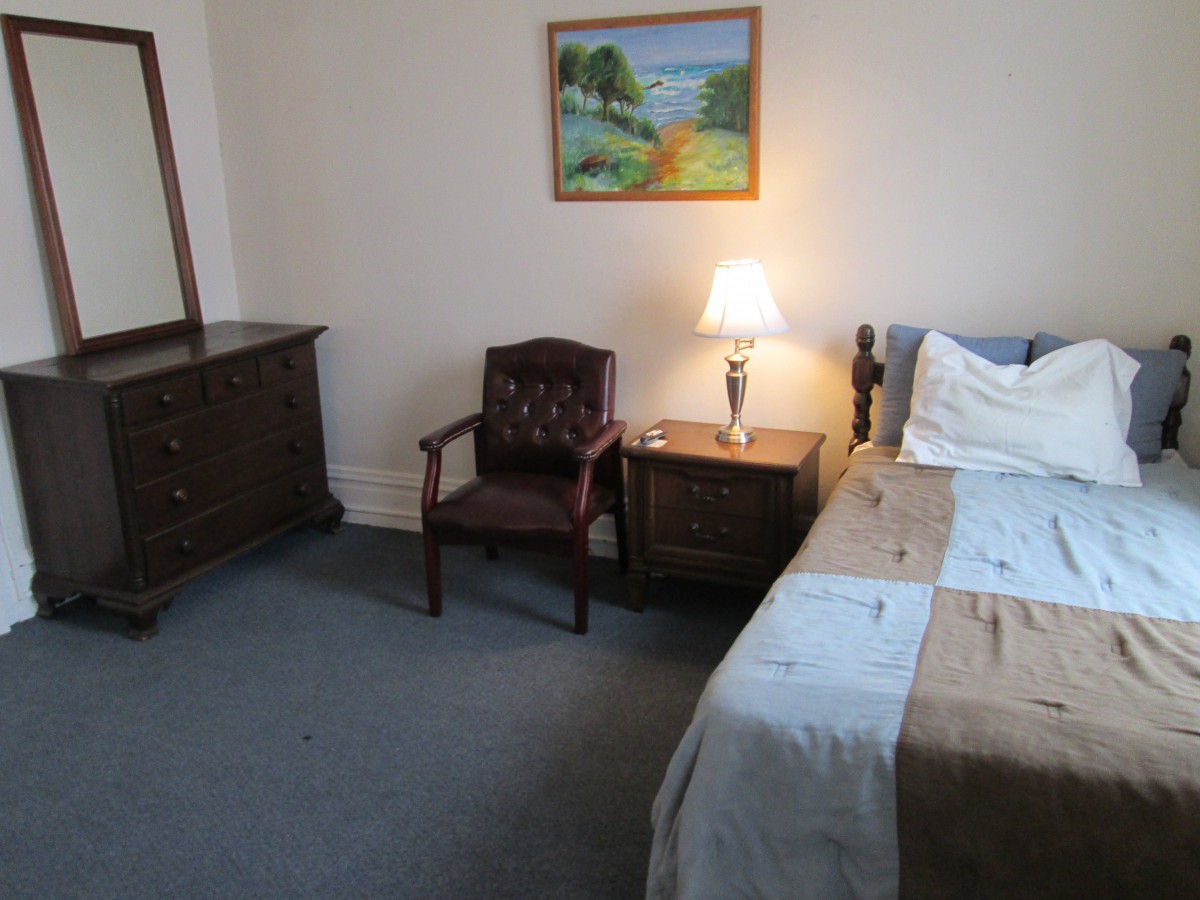 A cozy bedroom with a bed, dresser, chair, and a lamp on the nightstand.