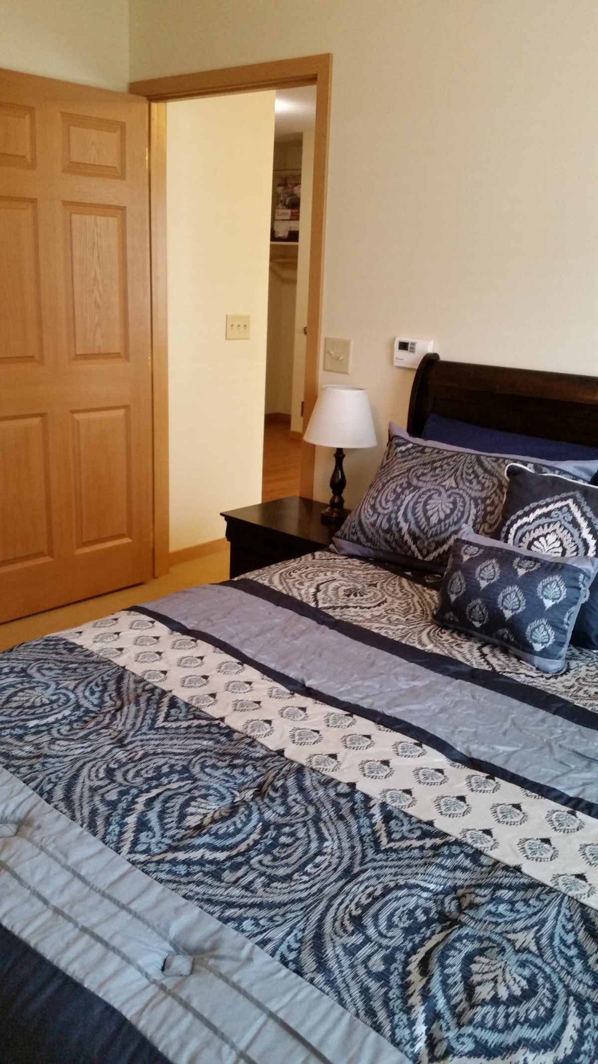 A cozy bedroom with a neatly made bed featuring patterned pillows and a bedside lamp.