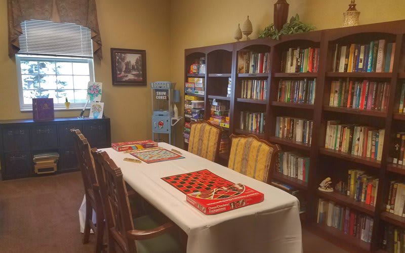 A cozy library room with bookshelves, a table set for checkers, and comfortable chairs.