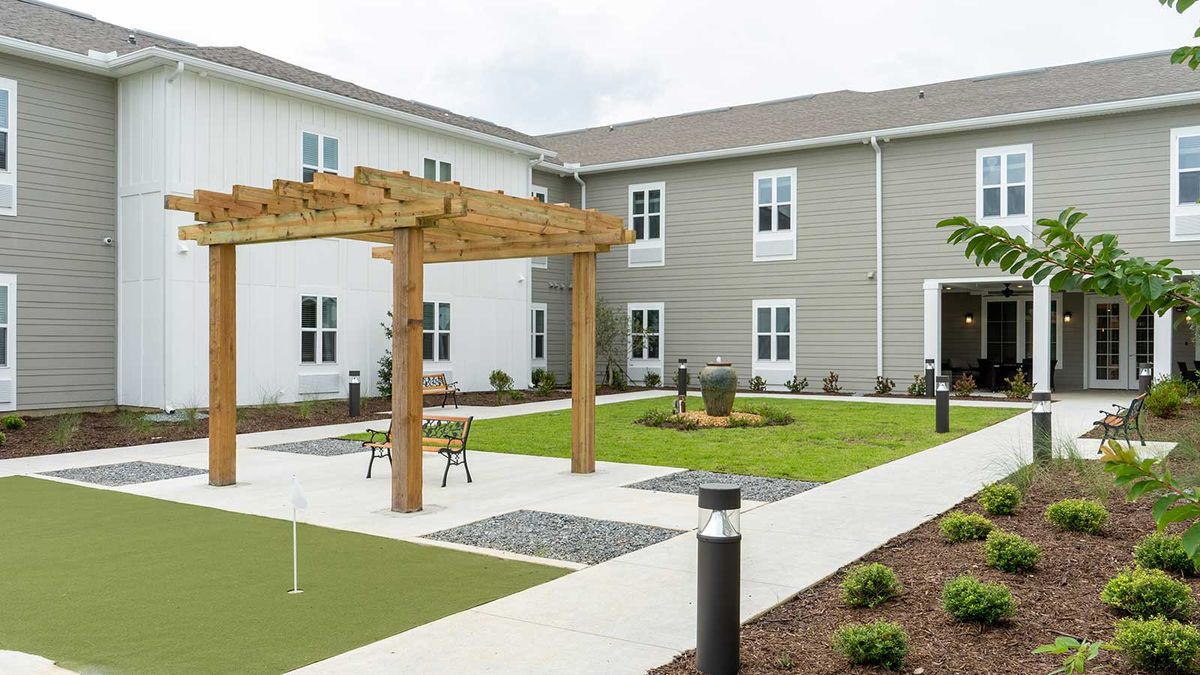 A modern courtyard with outdoor seating, a wooden pergola, and landscaped green space.
