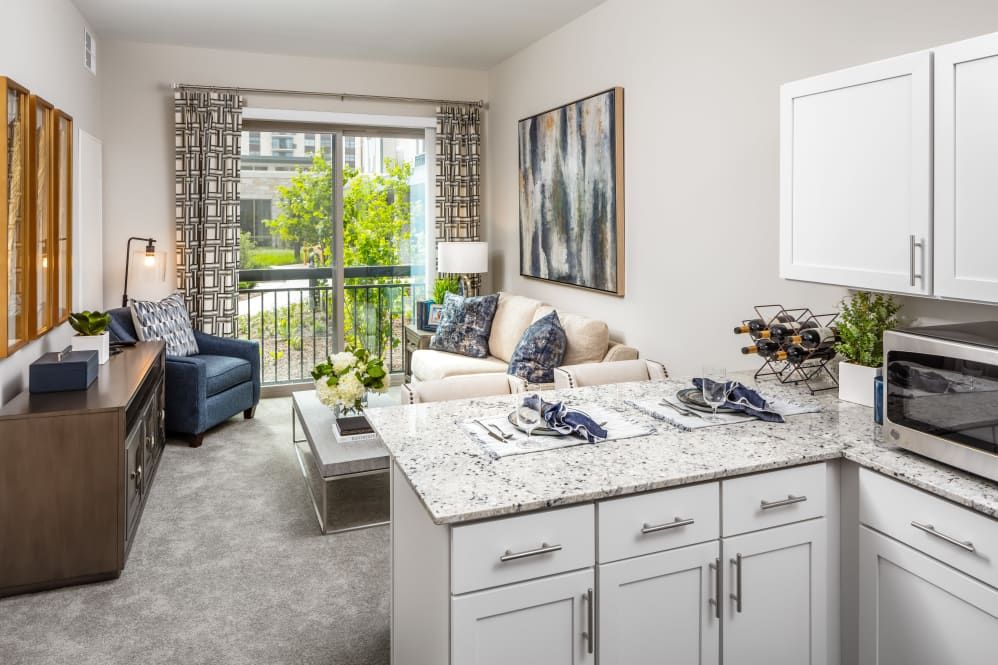A modern and elegantly decorated living room with a kitchen island, featuring stylish furniture and abundant natural light.