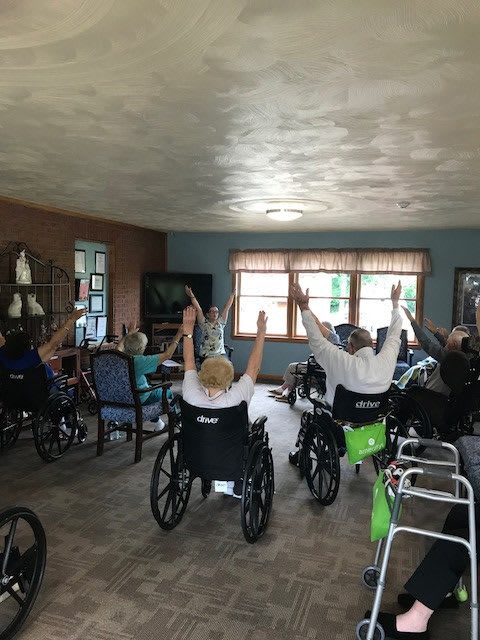 A group of elderly individuals participating in an indoor exercise session while seated in wheelchairs.