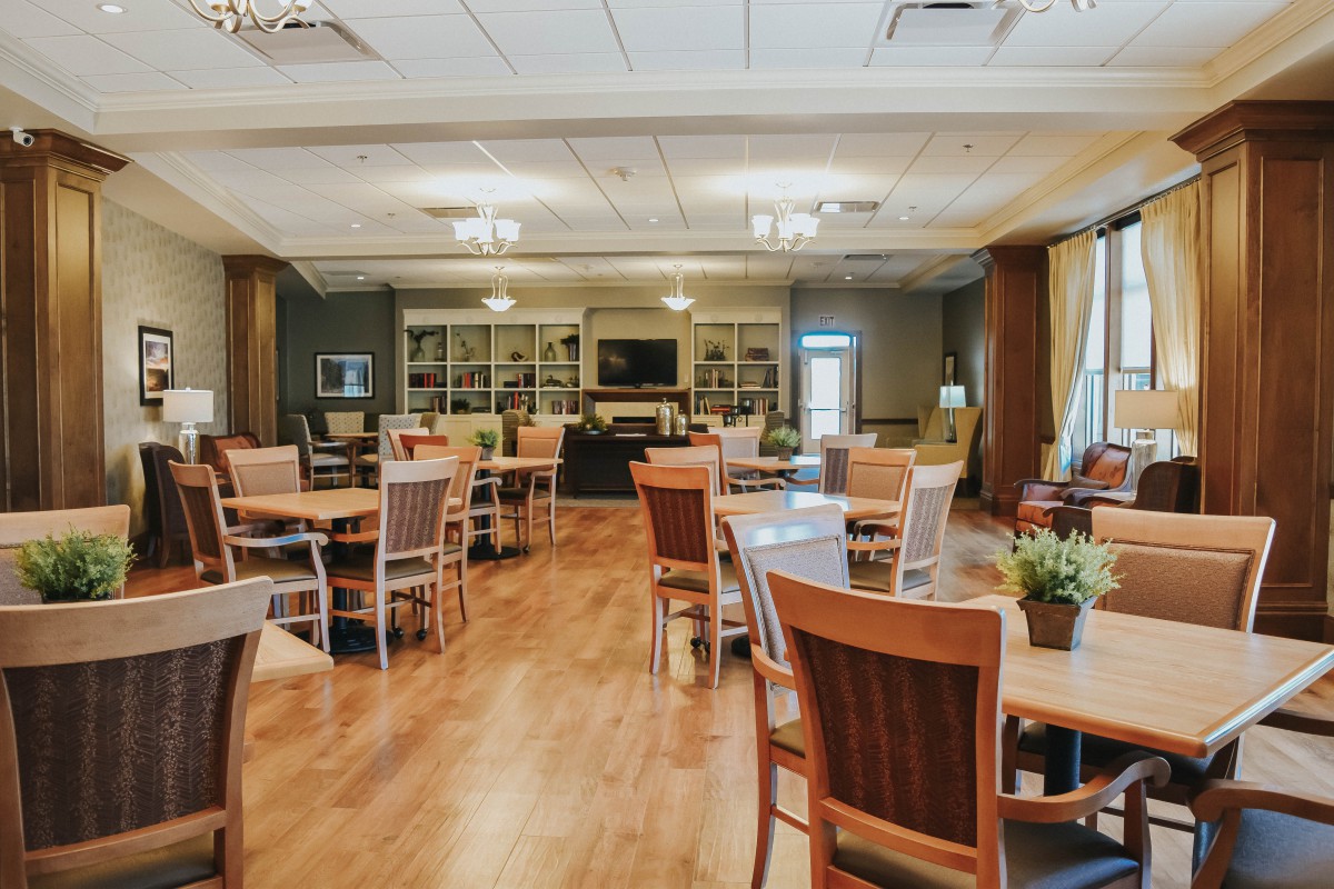 A spacious dining room with wooden tables and chairs, featuring elegant lighting and wood flooring.