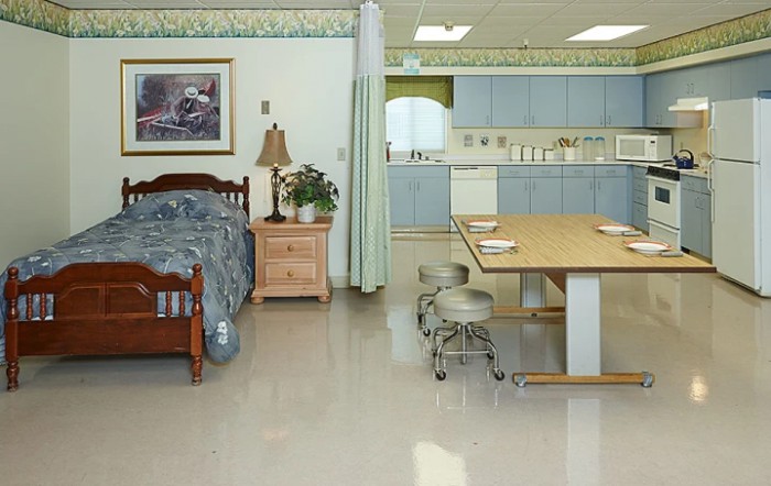 A room with a bed and a kitchen area, featuring wooden furniture and a dining table.