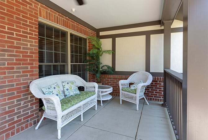 A cozy porch with wicker furniture and green cushions, featuring a small table and a potted plant.