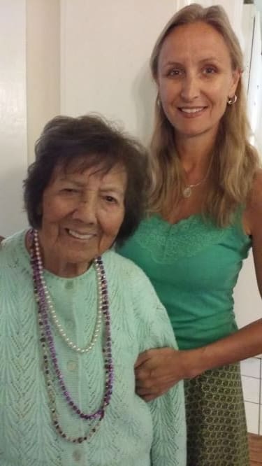 An elderly woman smiling alongside a younger woman indoors.