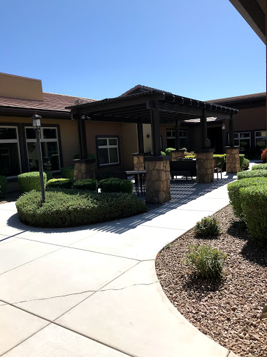 A view of a well-maintained building entrance with landscaped gardens and a shaded area.