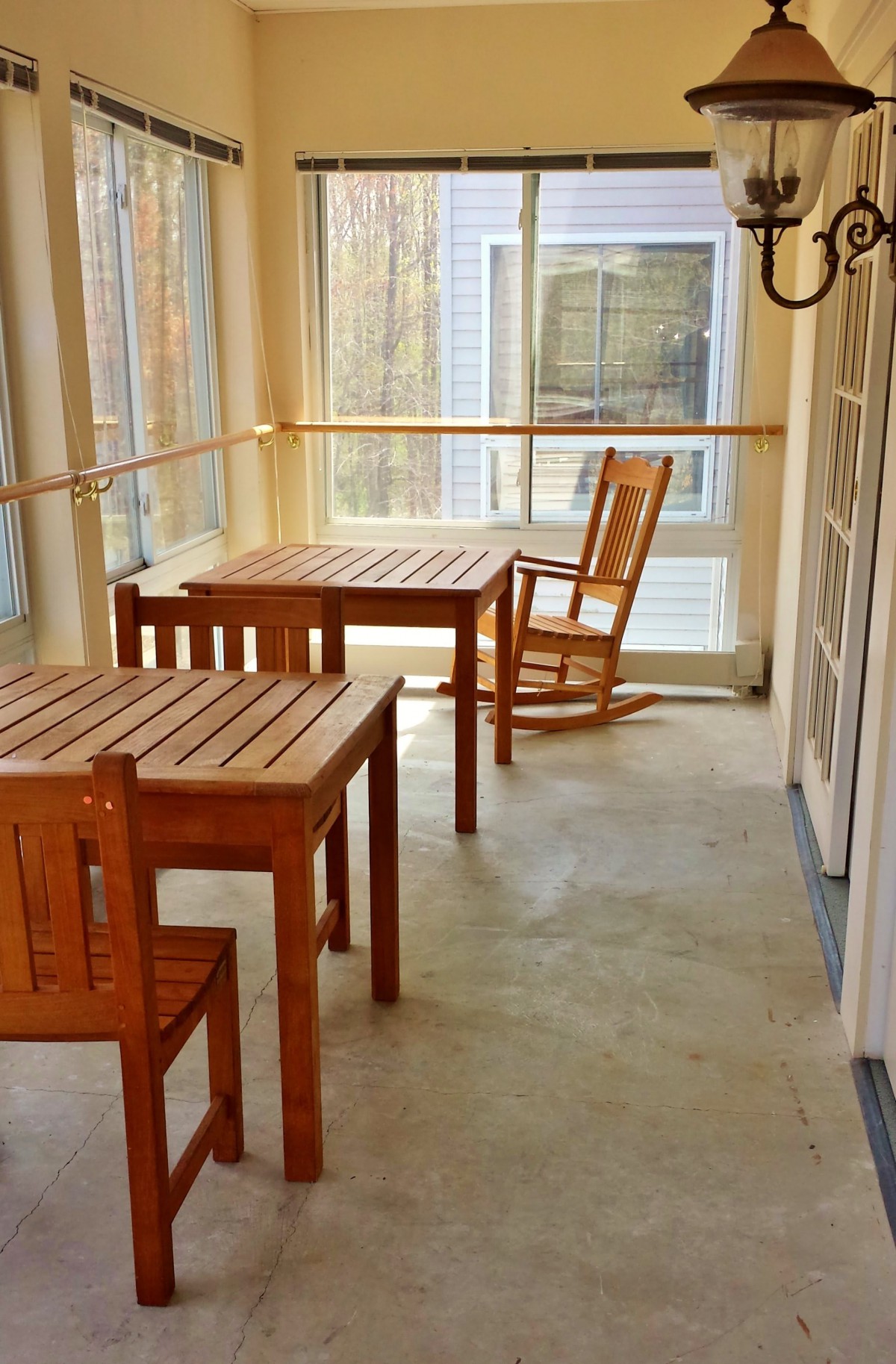 A sunlit room featuring wooden tables and chairs, including a cozy rocking chair.