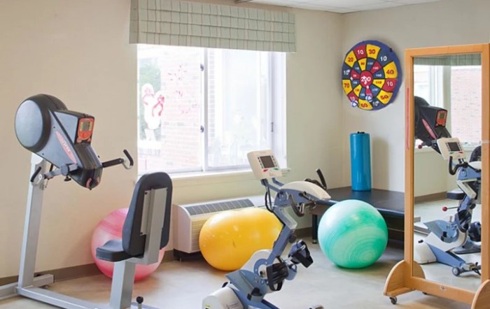 A small exercise room equipped with a stationary bike, colorful exercise balls, and a window providing natural light.
