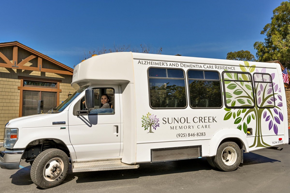 A white van featuring the logo and contact information of Senol Creek Memory Care, parked outdoors on a clear day.