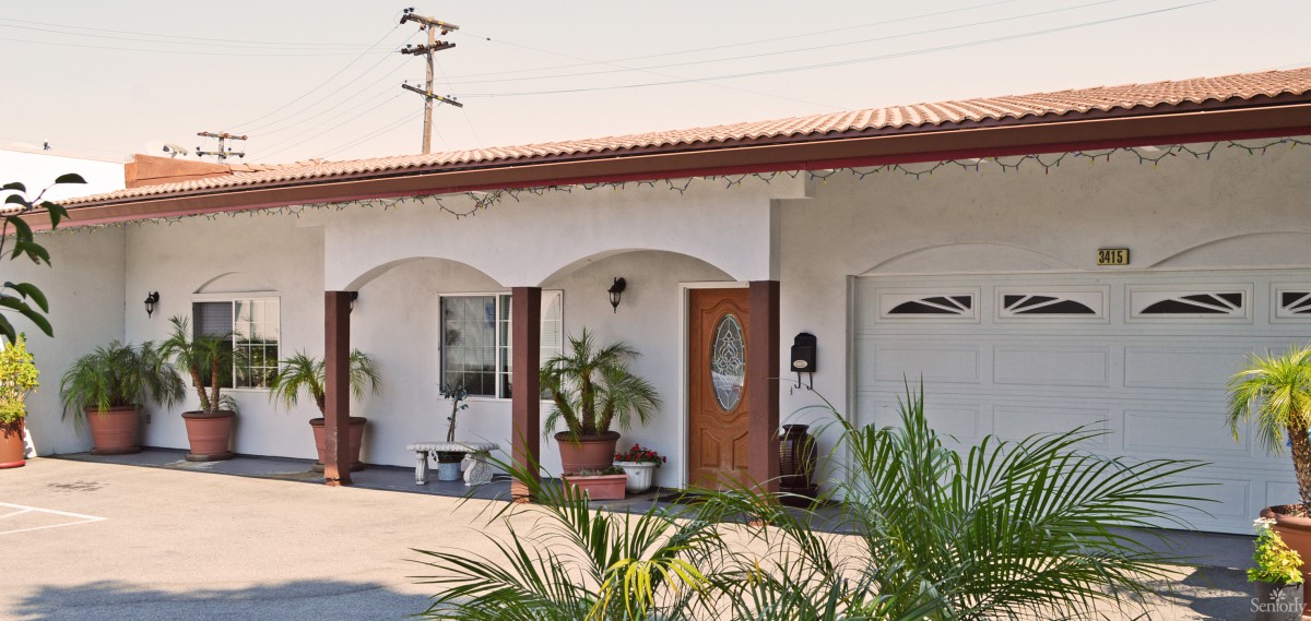 A single-story house with arched windows and doors, featuring potted plants in front.