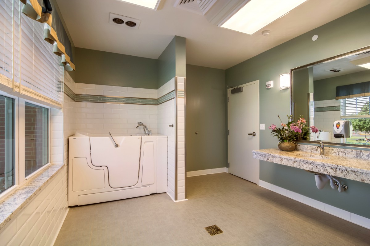 An accessible bathroom with a walk-in tub, sink, and mirror, featuring floral decorations.