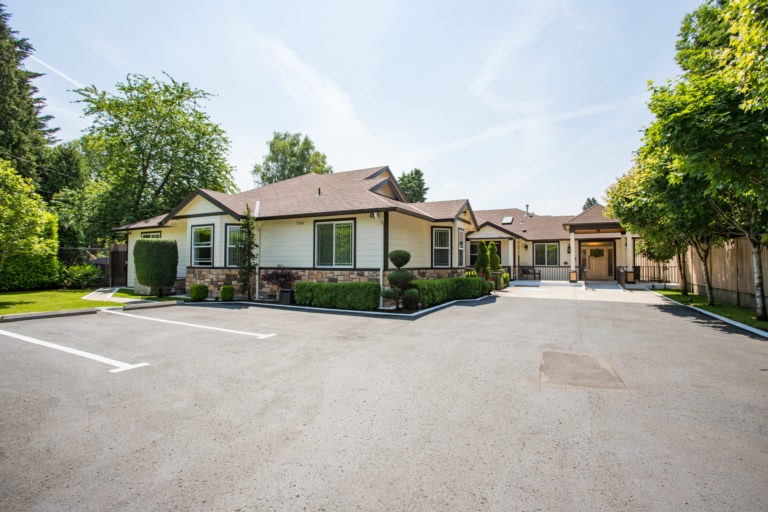 A suburban residential house with a driveway and surrounding greenery on a sunny day.