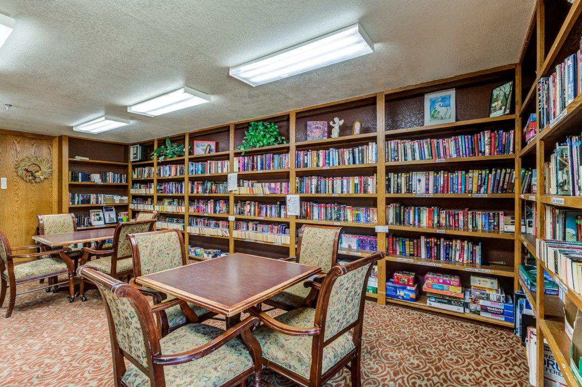 A cozy library interior with bookshelves filled with books and a wooden table surrounded by chairs.