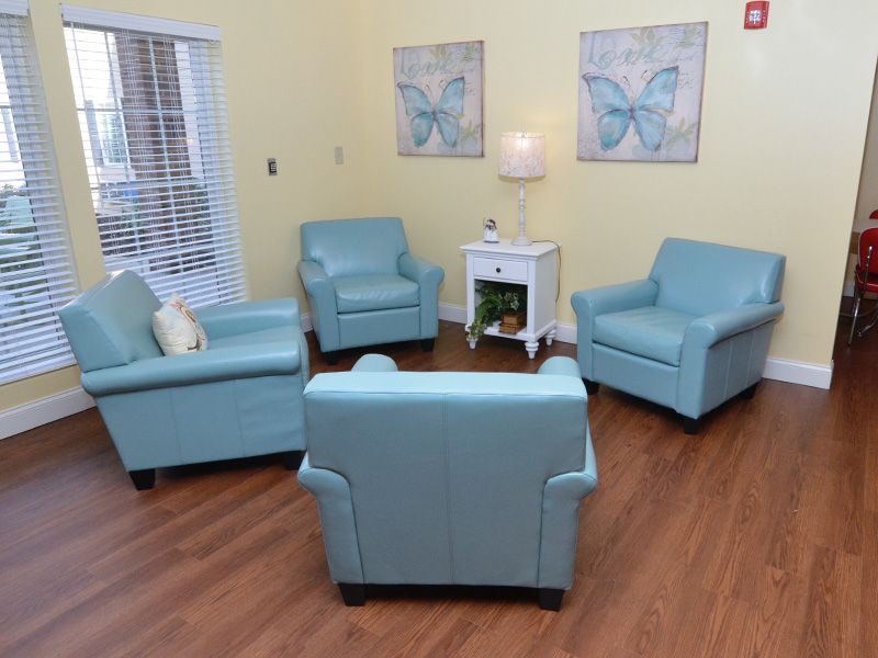 A cozy living room with four blue armchairs arranged in a circle, complemented by butterfly artwork on the walls and a small table with a lamp.