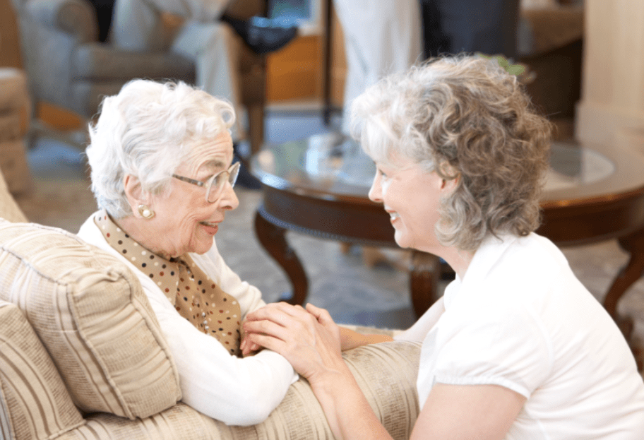 A younger woman engages in a comforting conversation with an elderly woman indoors.